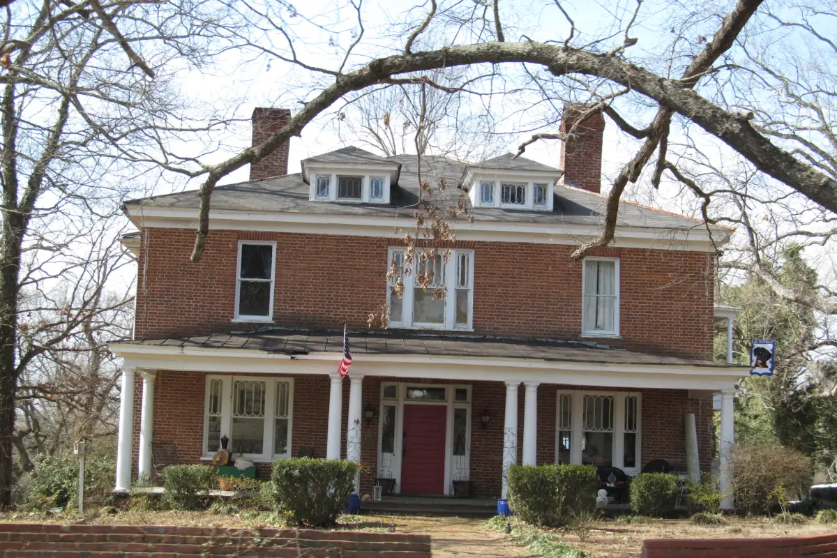 A brick house with a large shade tree on a street in Chatham, Virginia